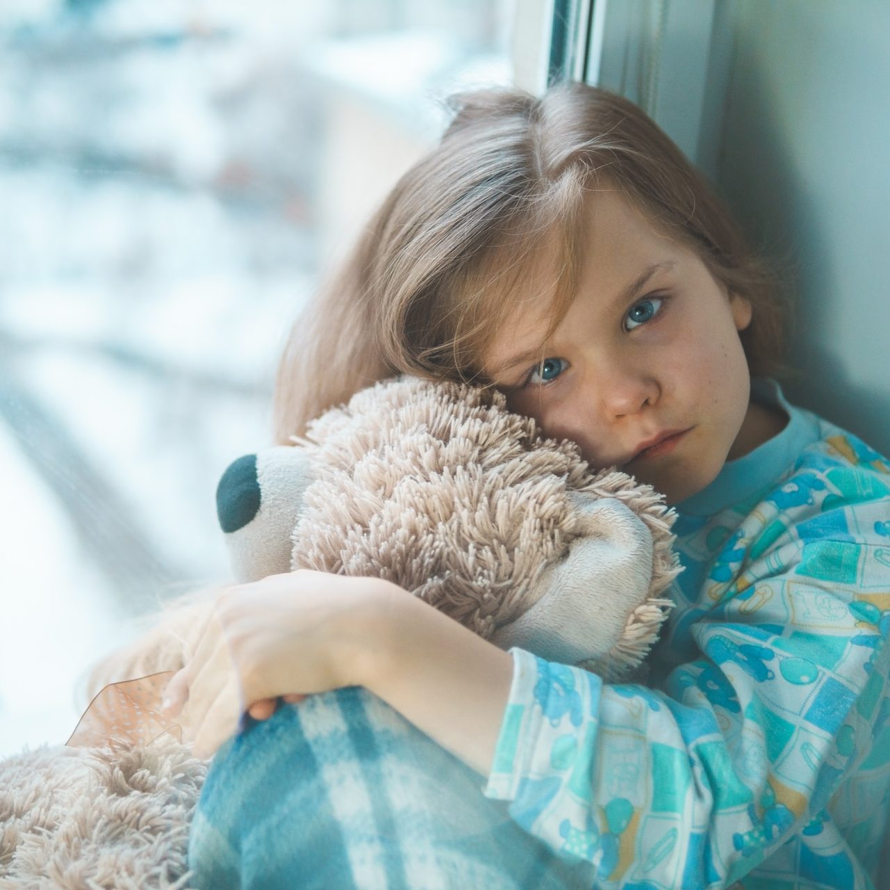 girl in blue white and red plaid shirt hugging brown teddy bear